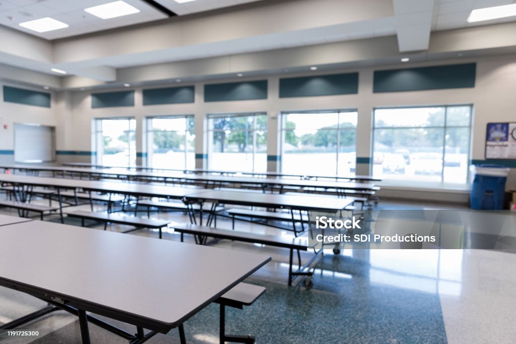 Clean, empty school cafeteria with large windows is ready for students.