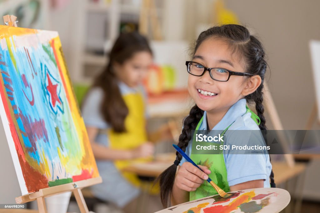 Beautiful Filipino elementary age art student smiles while working on a painting in art class.
